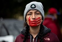 Woman with red handprint on her mouth, a symbol of solidarity with missing and murdered Indigenous women and girls