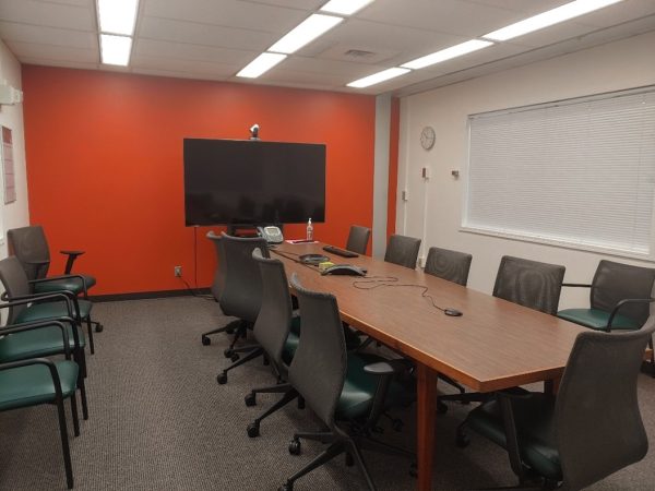 Photo of Room T223 showing a long conference tab, TV and offices chairs