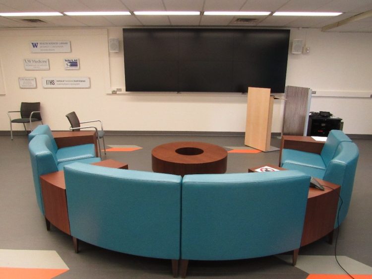 A semi-circular seating area with a tables and a large screen on the wall.