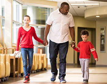 A man holding the hands of two children as they walk down a hall.