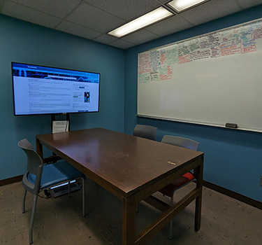 Room with a table, chairs, whiteboard and large monitor on the wall.