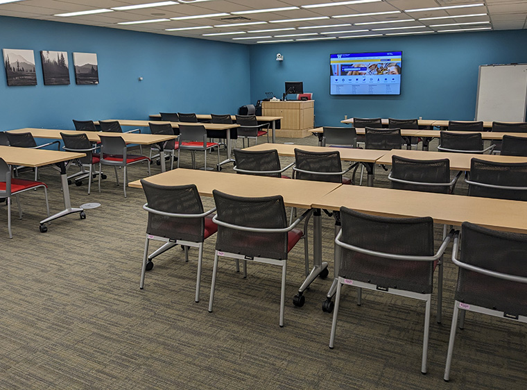 Large room with eight double tables with four chairs each, wall monitors and whiteboard.