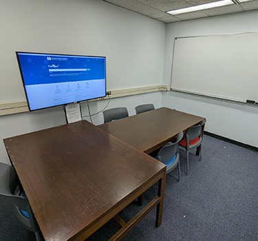 Study room with two tables with chairs and a tv monitor.