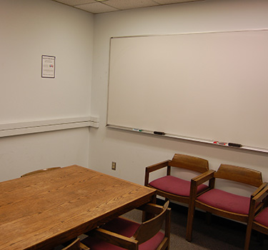 A quiet study area with a door, a whiteboard, and a wooden table with chairs.