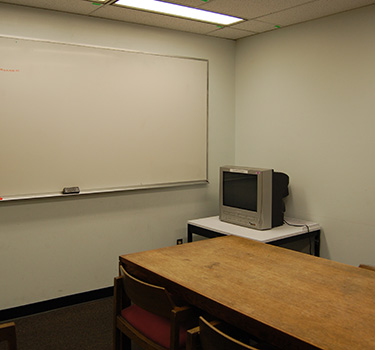 A quiet study area with a door, a whiteboard and a wooden table with four chairs.