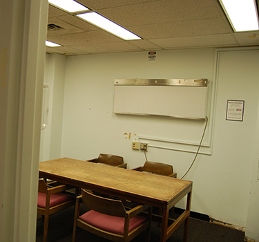 Quiet study area with a door, wooden table with four chairs and a whiteboard.