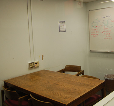 A room with a door, electric outlet, whiteboard and a table and four chairs.