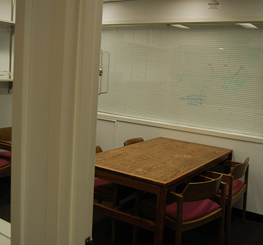 A quiet study room with a door, outlets, a white board and wooden table with four chairs.