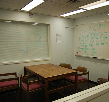 Study room with a door, whiteboard, electric outlet and a table and four chairs.