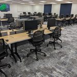Tables, chairs and computers arranged in rows with an aisle down the center in the HSL Commons