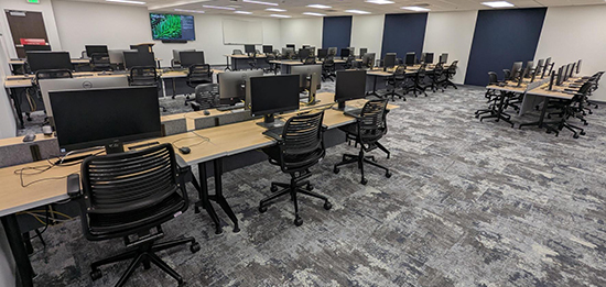 Tables, chairs and computers arranged in rows with an aisle down the center in the HSL Commons