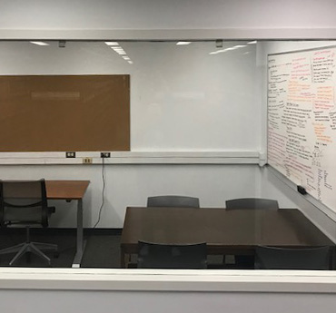 Study room with an adjustable height table, a wood table with four chairs around it, and a whiteboard on the wall