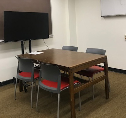 Study room with a wood table with four chairs around it and a large television