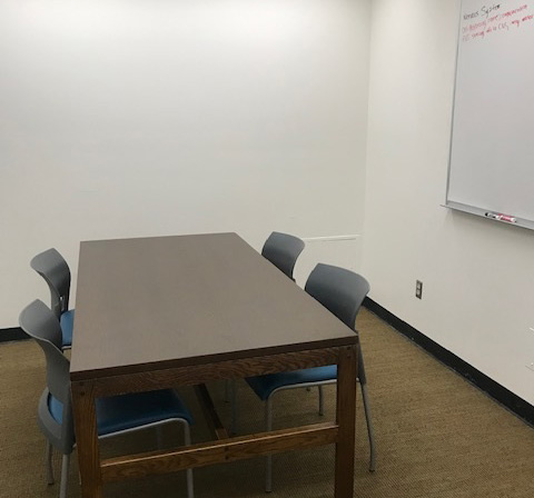 Study room with a wood table with four chairs around it and a whiteboard on the wall